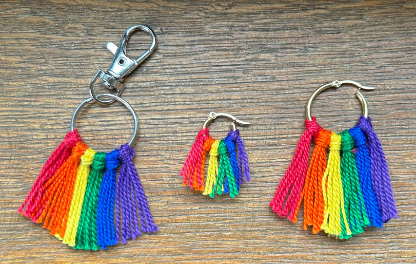 Two sizes of rainbow tassel earrings and a keychain on a wood surface